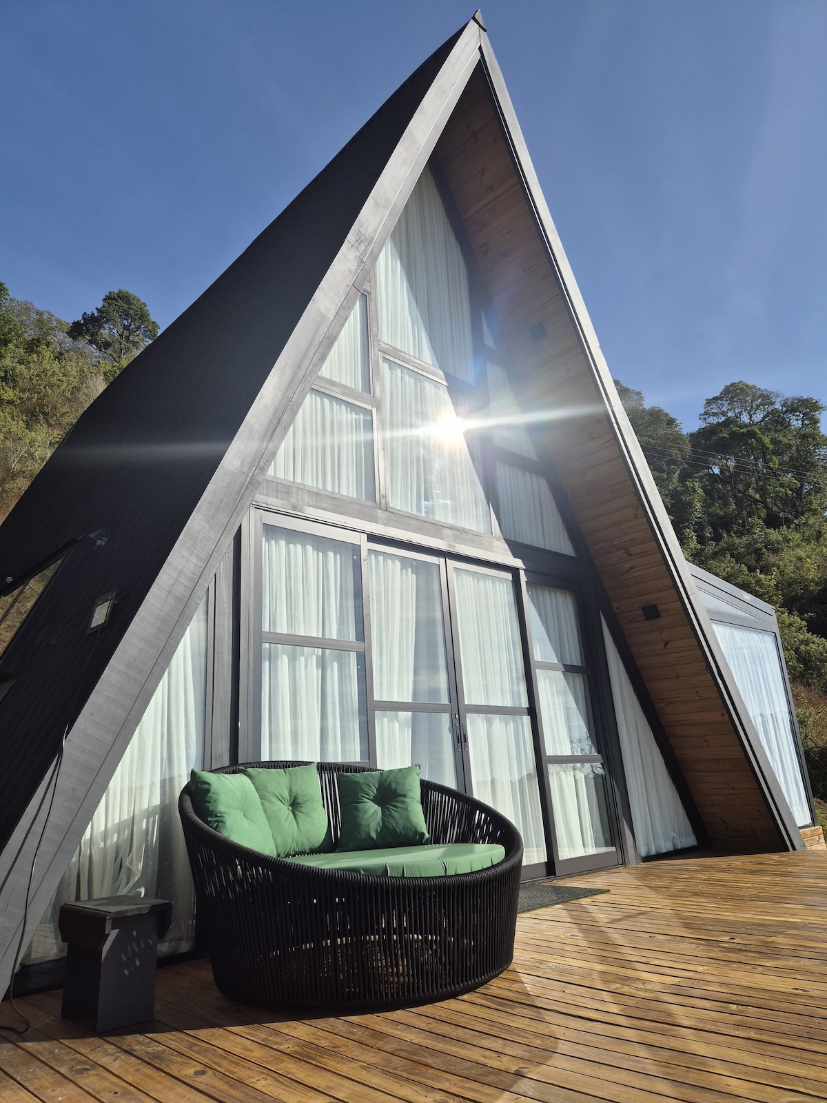 Fachada da cabana A-frame, com poltrona verde no deck de madeira